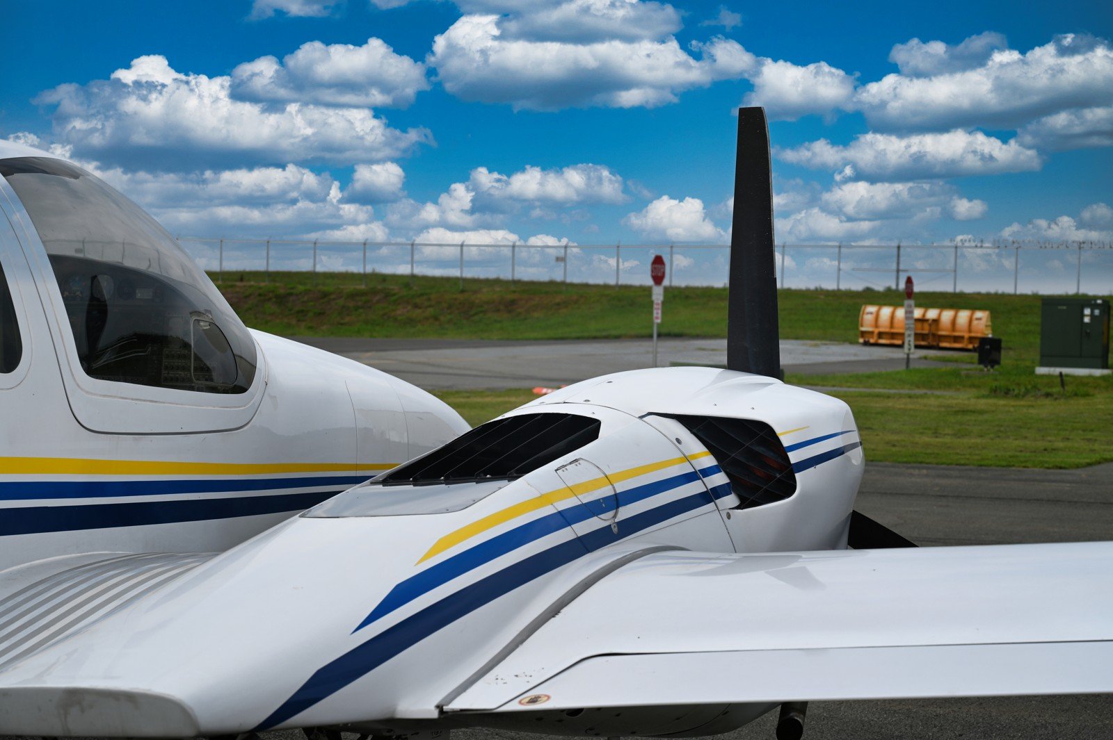Nose and propeller of a Diamond with blue and gold stripes under clouds