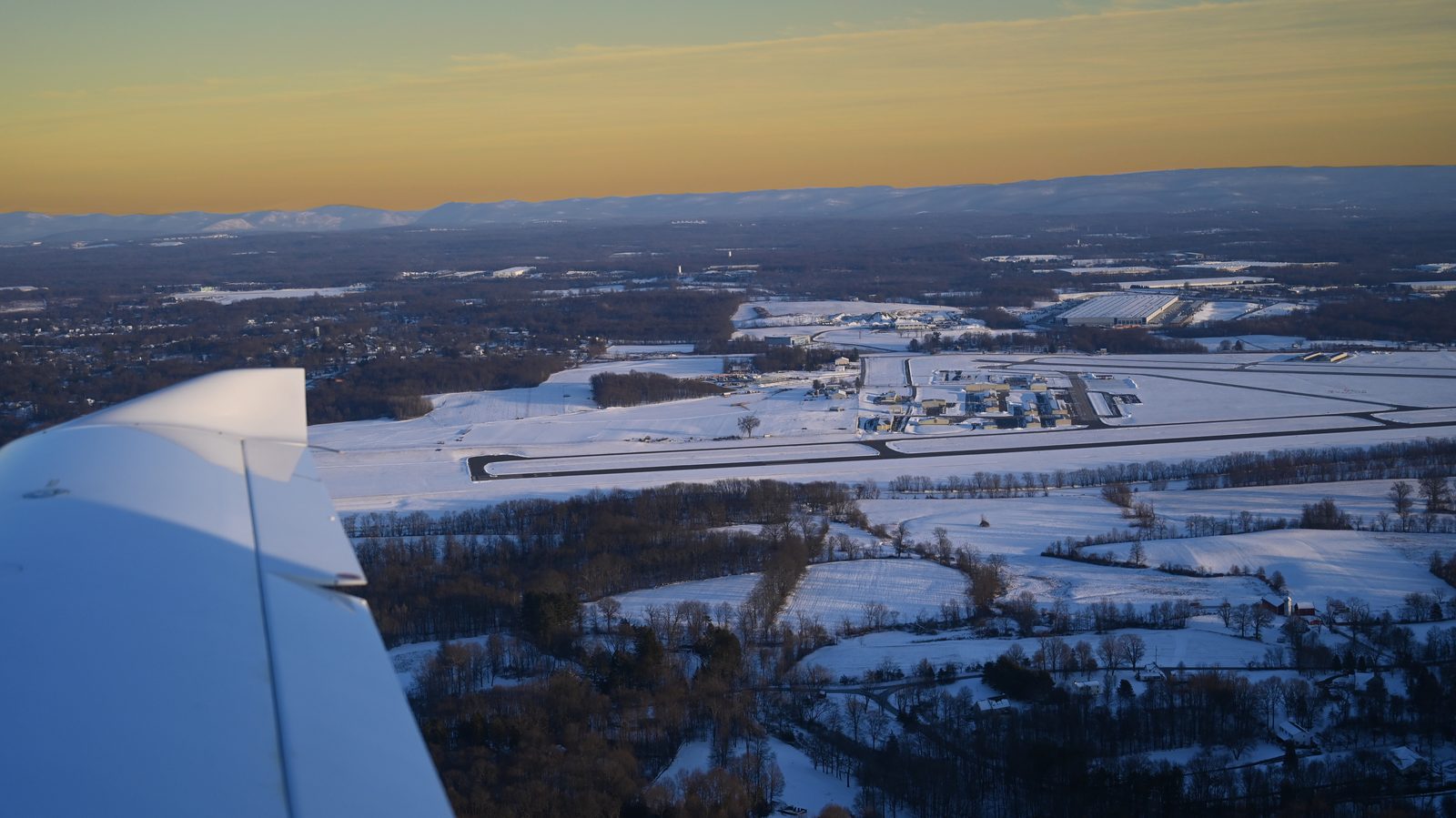Snowy farmland seen past the wing at sunset